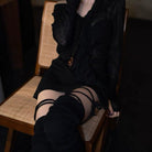 Person wearing a black dress and stockings sitting on a wooden chair.