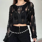 Person wearing a black, sheer long-sleeve top with cut-out designs against a plain background.