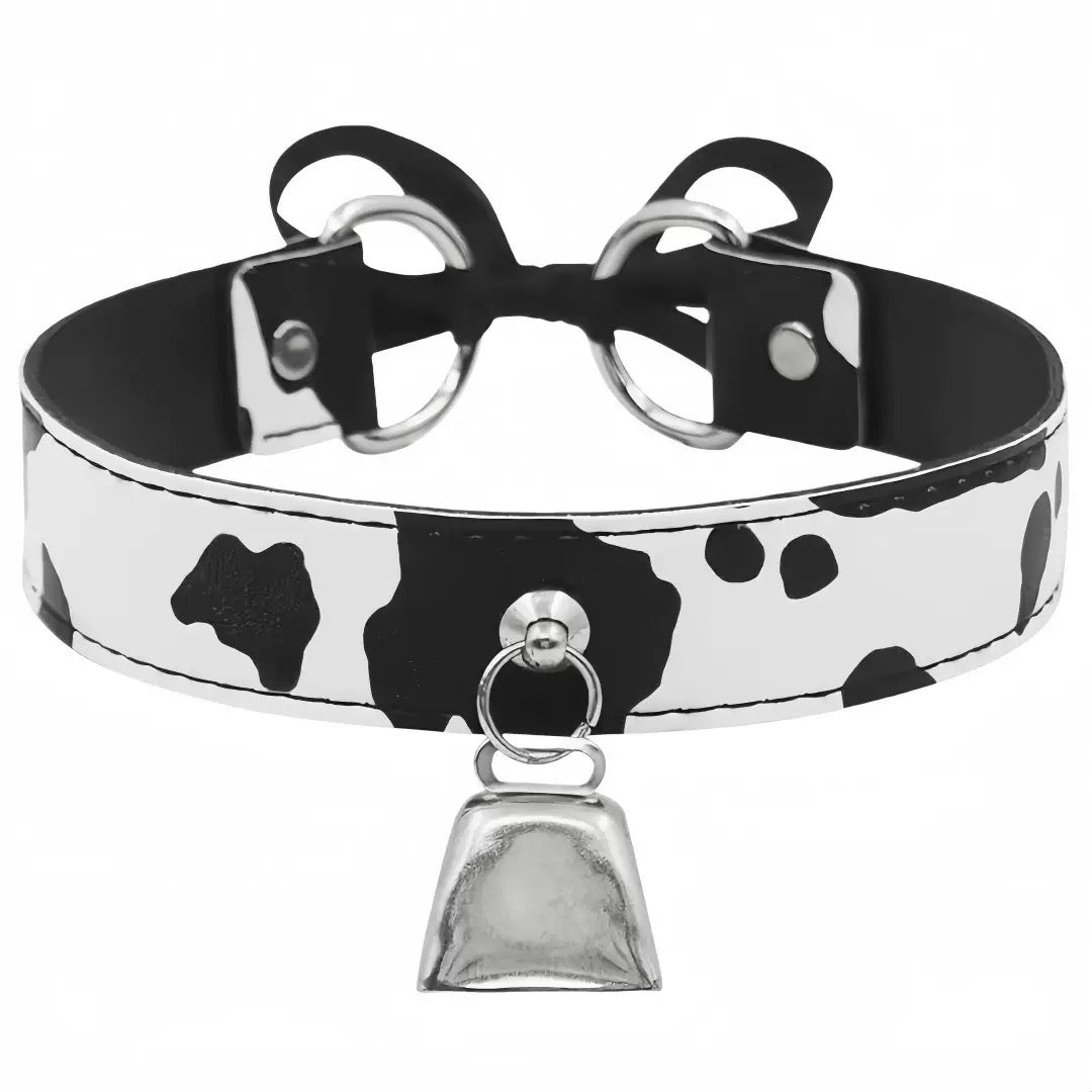 A black and white cow-print faux leather choker collar with silver-tone metal hardware, featuring a bow at the back and a dangling bell charm.