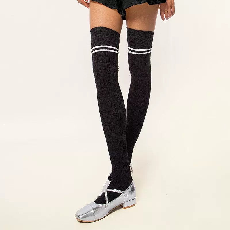 Black thigh-high socks with white stripes worn by a person on a light background