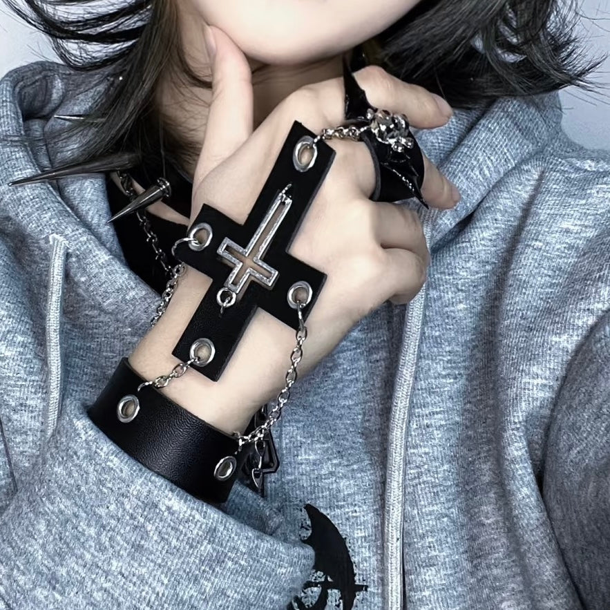 Person wearing a black gothic cross skull ring chain bracelet on a gray background