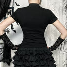 Person wearing a black dress with a ruffled skirt and black gloves in front of a decorative background.