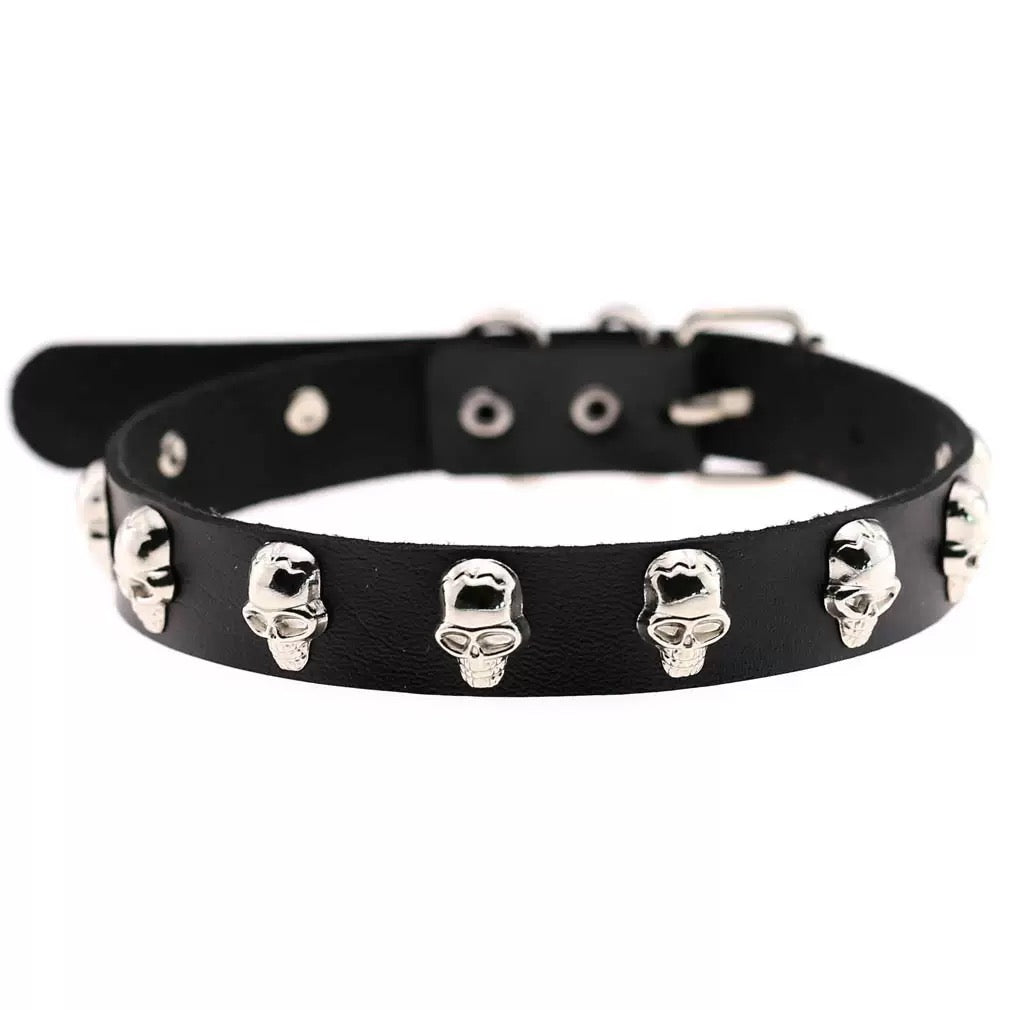 A black leather collar decorated with multiple silver skull studs, displayed against a plain white background.