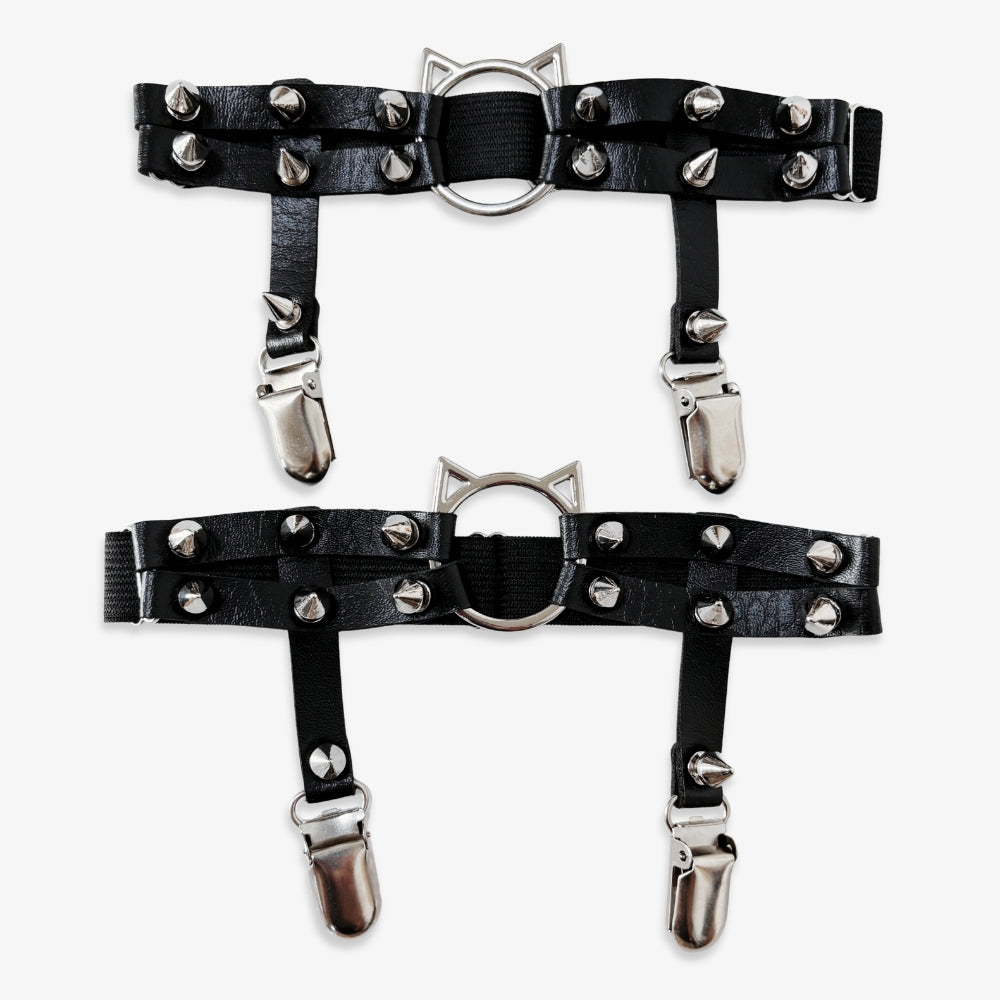 Black leather leg garters with silver studs and clips on a white background