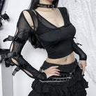 Person wearing a black outfit with sheer sleeves and a skirt against a white background