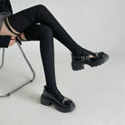 Person wearing black platform shoes with buckles on a light gray background