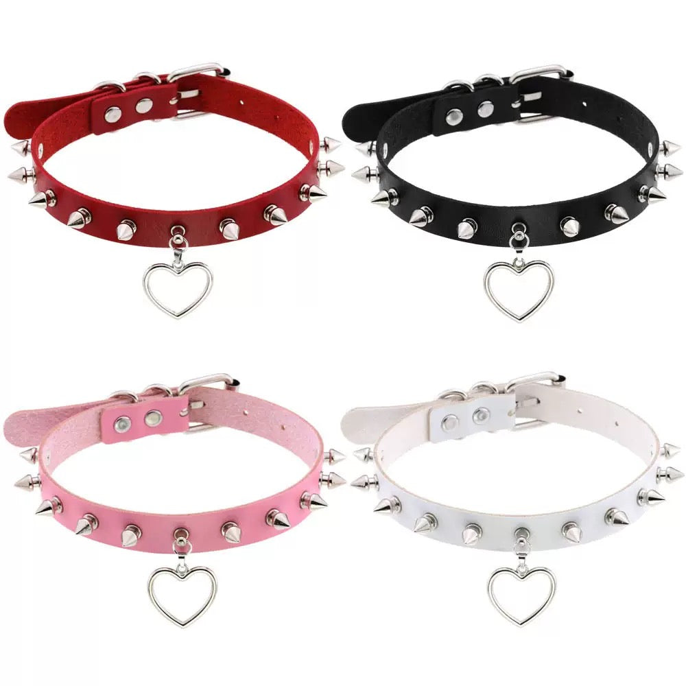 Four spiked chokers in red, black, pink, and white with heart-shaped charms on a white background.
