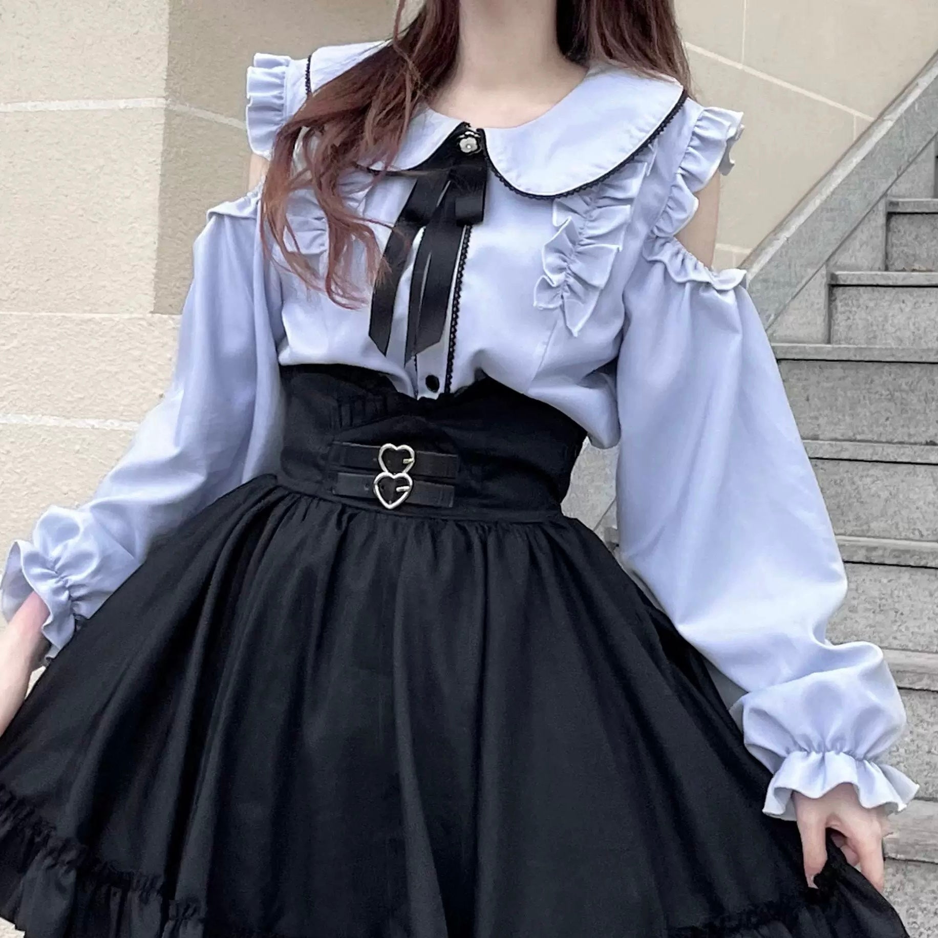 Woman wearing a blue long-sleeve top with cut-out design and black pants on a white background