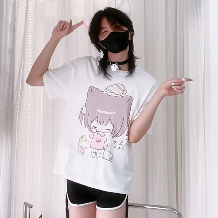 Person wearing a white t-shirt with a cartoon character design, posing in front of a white curtain.