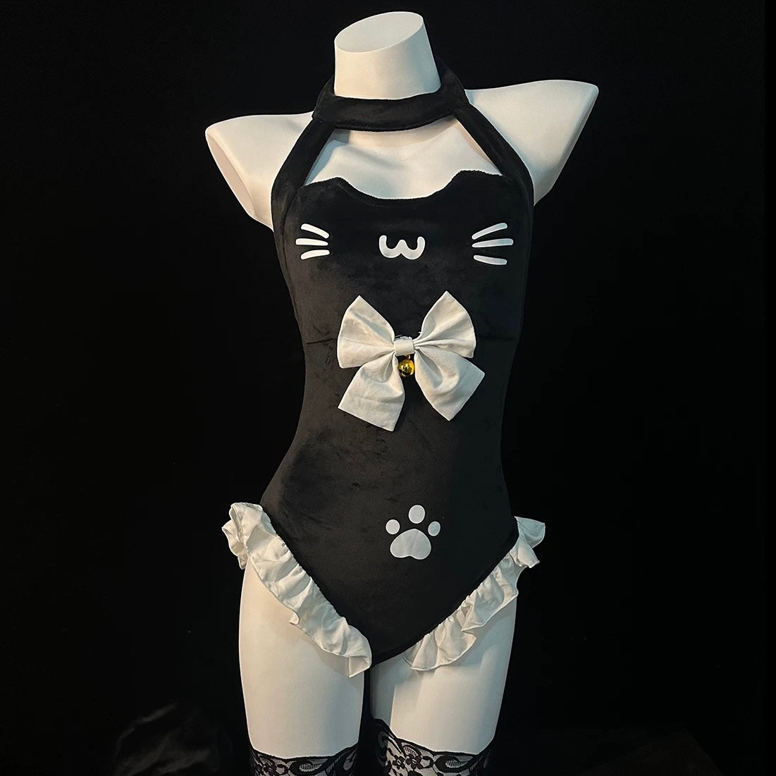 A black cat-themed halter bodysuit with white ruffles, a large white bow with a small bell, and white cat face and paw print graphics, displayed on a white mannequin torso against a black background.