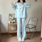 Person wearing a light blue pajama set taking a mirror selfie in a room with a wooden shelf and chair.