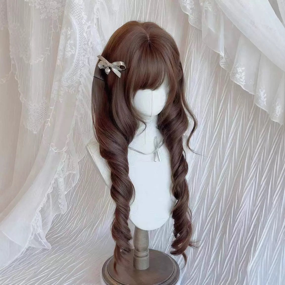 Femboy chocolate brown elegant curl wig with a bow on a mannequin head against a white lace curtain background