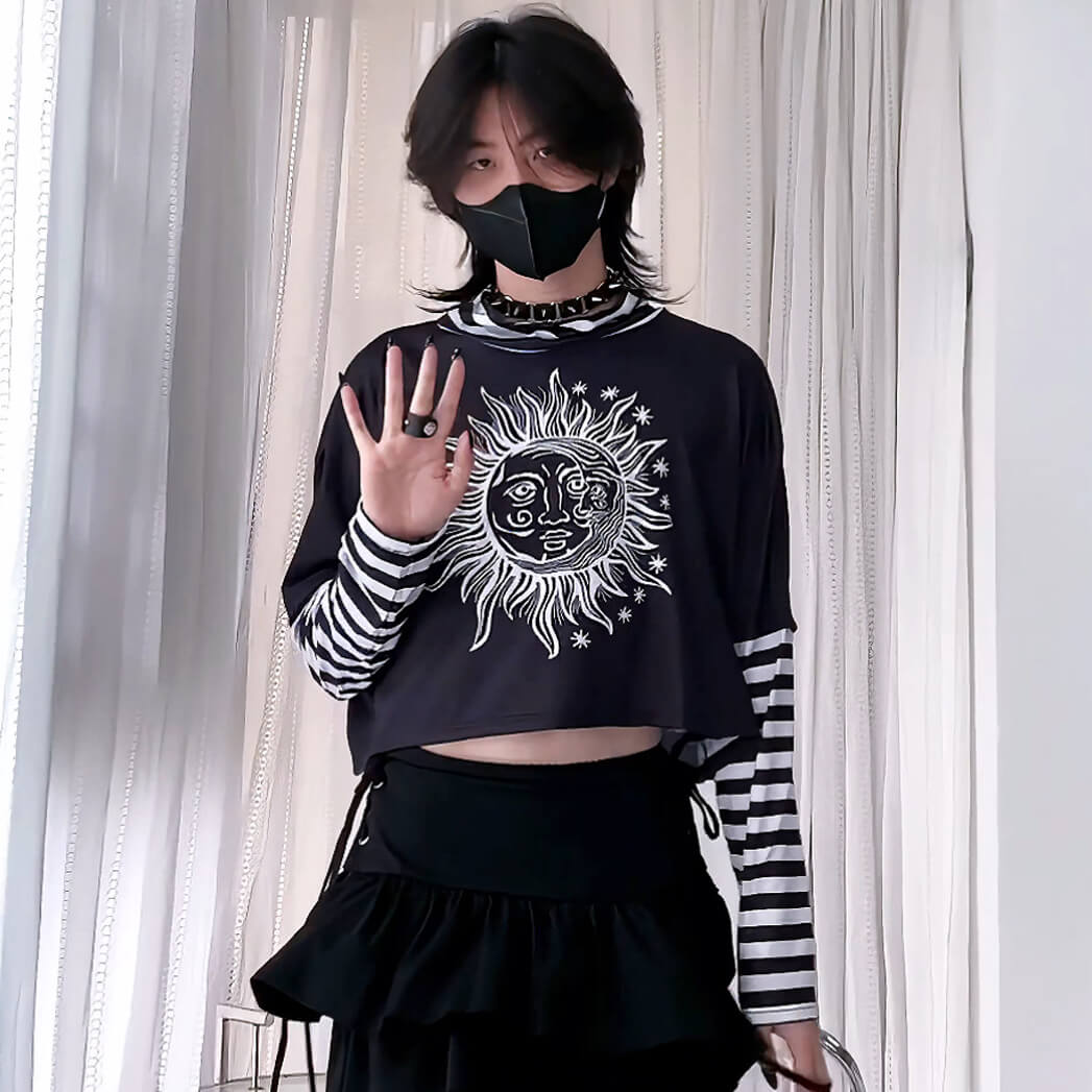 Person wearing a black crop top with a sun and moon design, black skirt, and striped sleeves against a white curtain background.