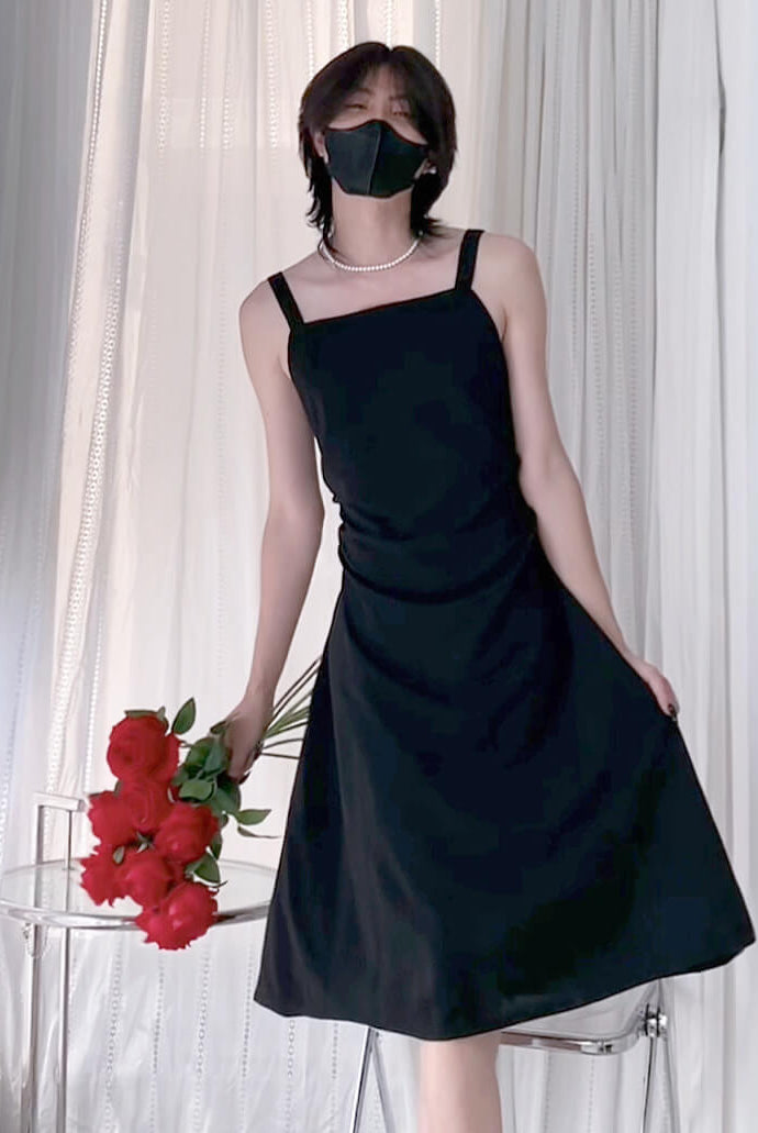 Femboy in a black dress holding red flowers against a white curtain background