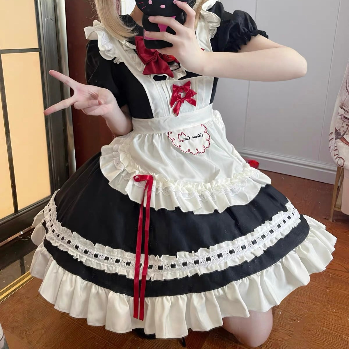 Person wearing a black and white maid outfit with red accents, posing indoors.