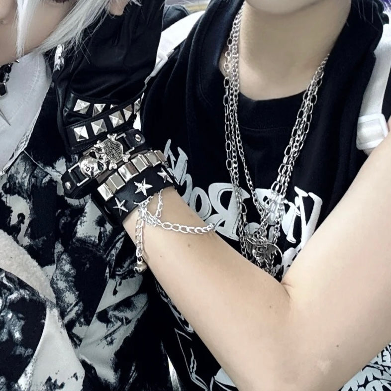 Person wearing gothic skull leather bracelets and a necklace with a black and white patterned background