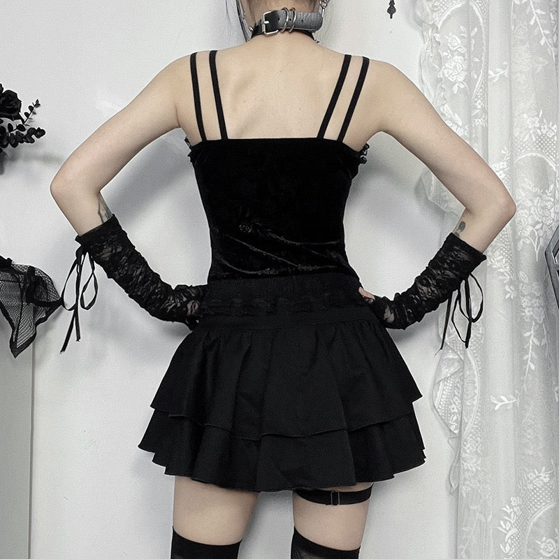Person wearing a black gothic zip-up corset top with thin straps and a tiered skirt, standing against a white curtain.