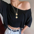 Femboy wearing a black off-shoulder top and white pants with a gold necklace.