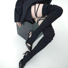 Person wearing black pants, black shoes, and sheer stockings with black straps on a white background