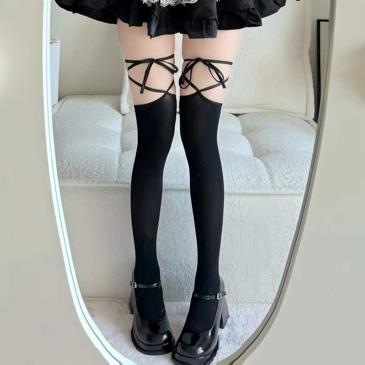 Person wearing black pants, black shoes, and sheer stockings with black straps on a white background