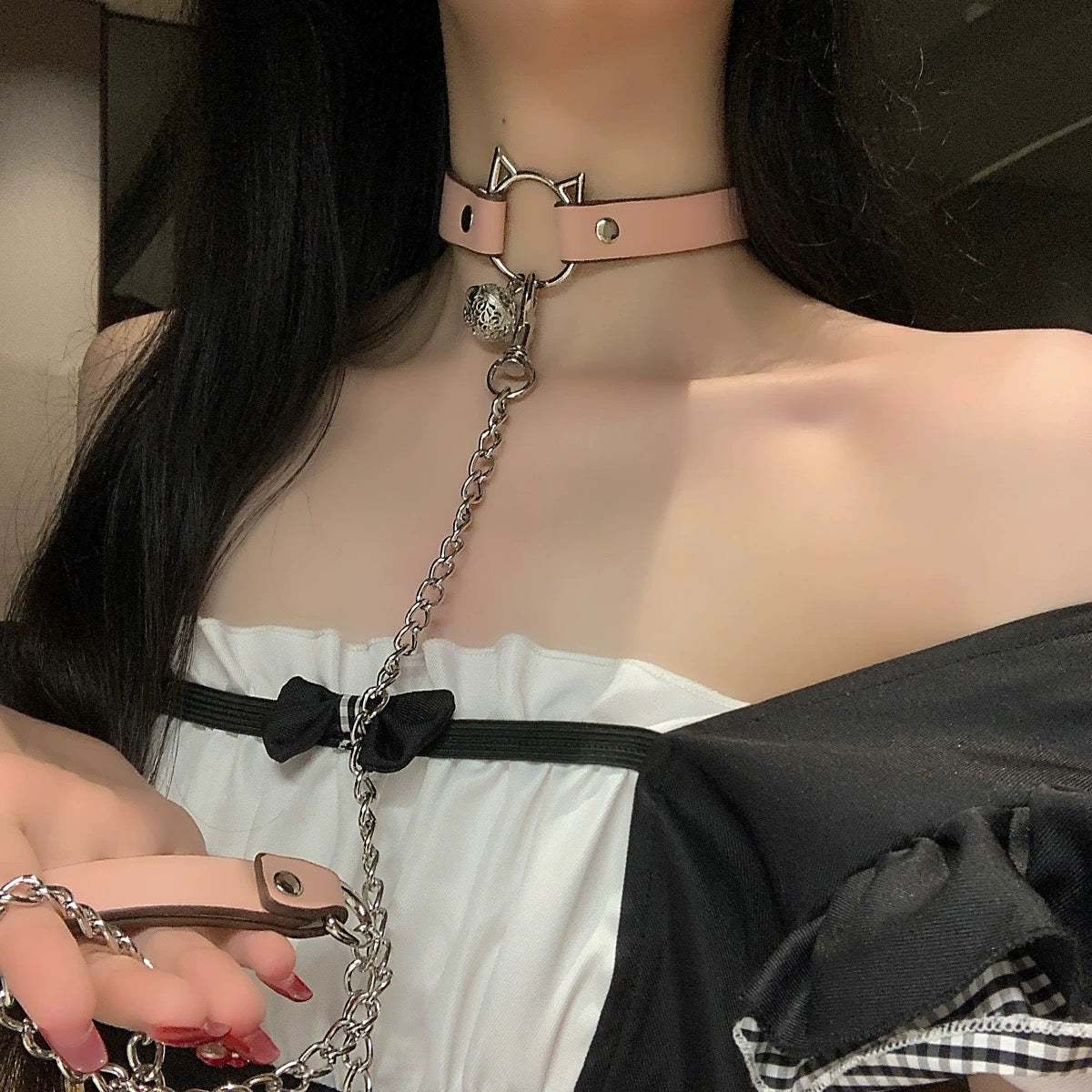 Person wearing a pink cat-shaped leather choker with a chain, holding a leather chain