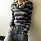 Person wearing a black and gray striped sweater and blue jeans against a plain wall.