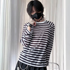 Person wearing a black and white striped long-sleeve shirt in front of sheer curtains.