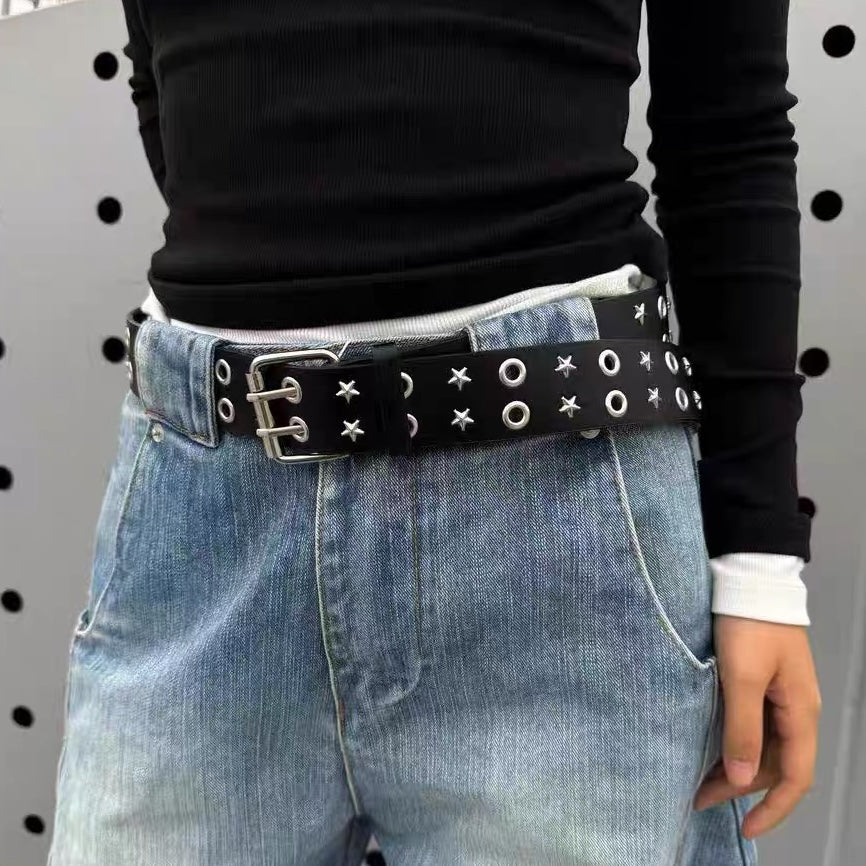 Person wearing a black belt with star patterns on blue jeans against a gray background