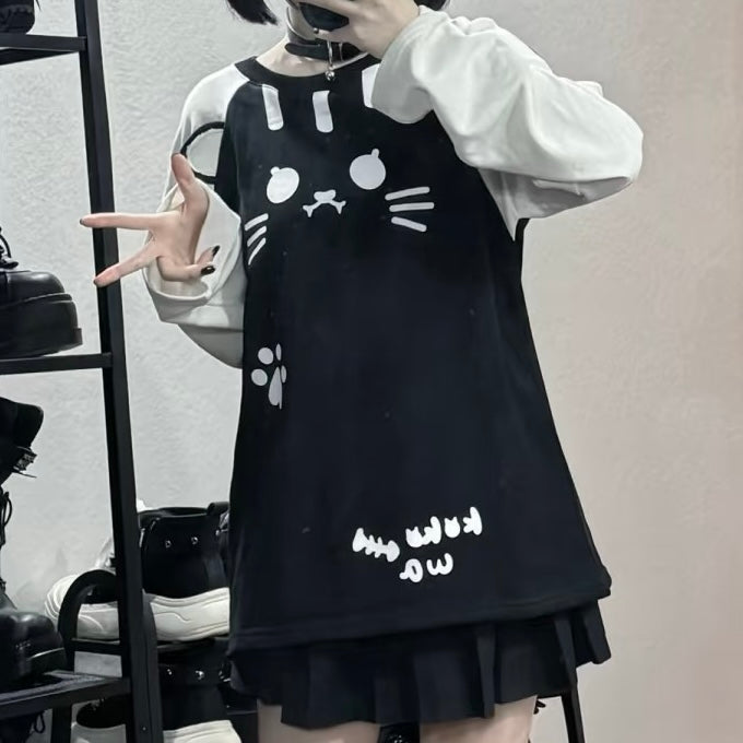 A femboy wearing a black cat-face print mini dress over a white long-sleeve shirt, standing in front of a mirror with shoes on a shelf in the background.