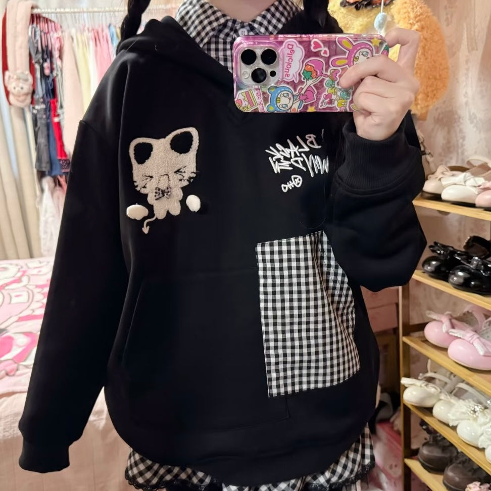 Person wearing a black hoodie with a cat design and checkered pattern, taking a selfie in a store.