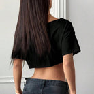 Person wearing a black crop top and dark jeans with long hair, standing against a neutral background.