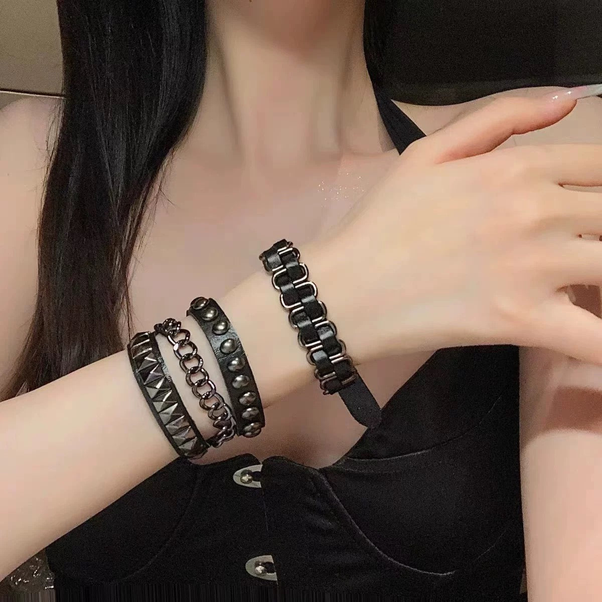 Person wearing black punk pu leather bracelets set on a plain background