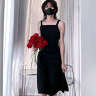 Femboy wearing a black dress and holding red roses in front of white curtains