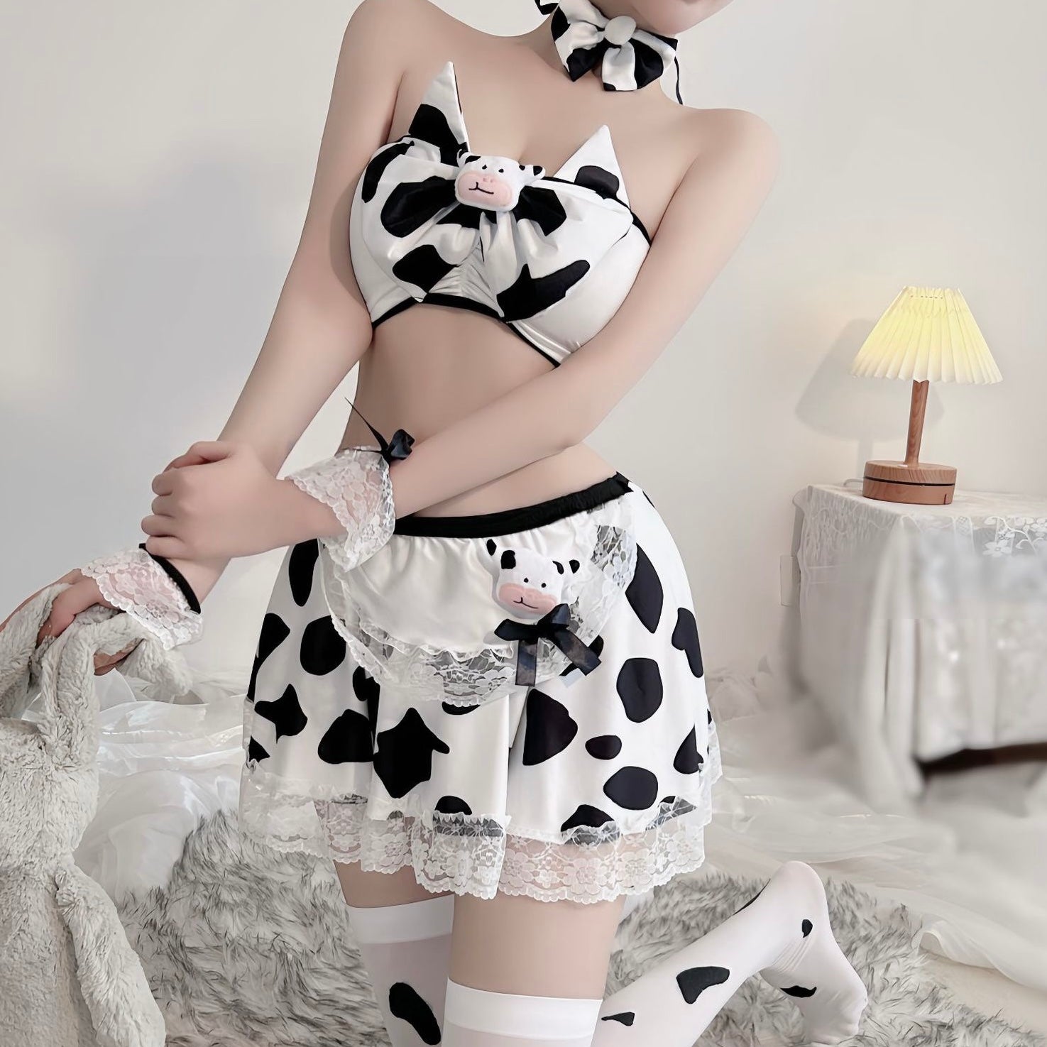 Person wearing a cow print outfit with a skirt and top, sitting on a bed.