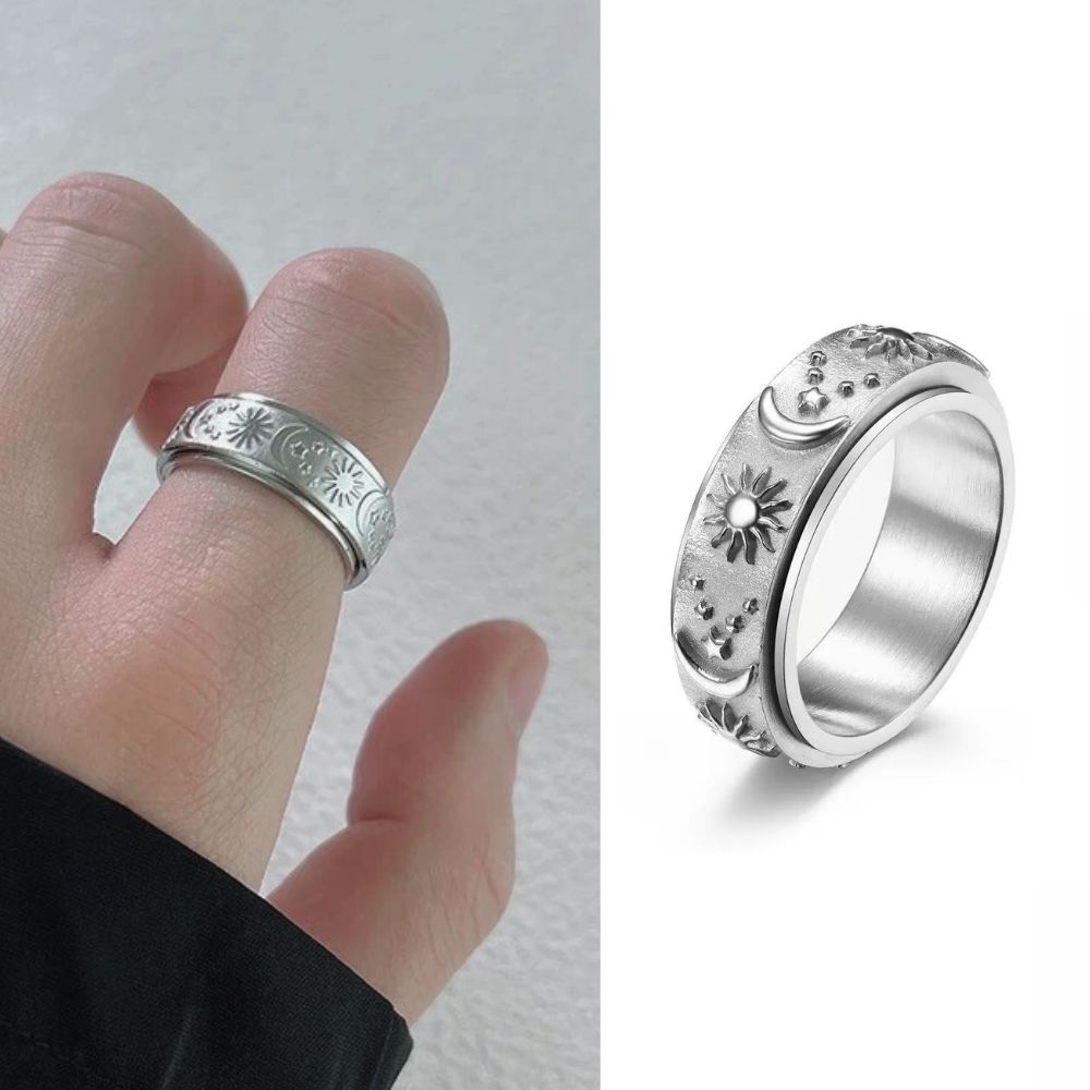 Silver ring with engraved design worn on a finger and shown from a side angle on a white background.