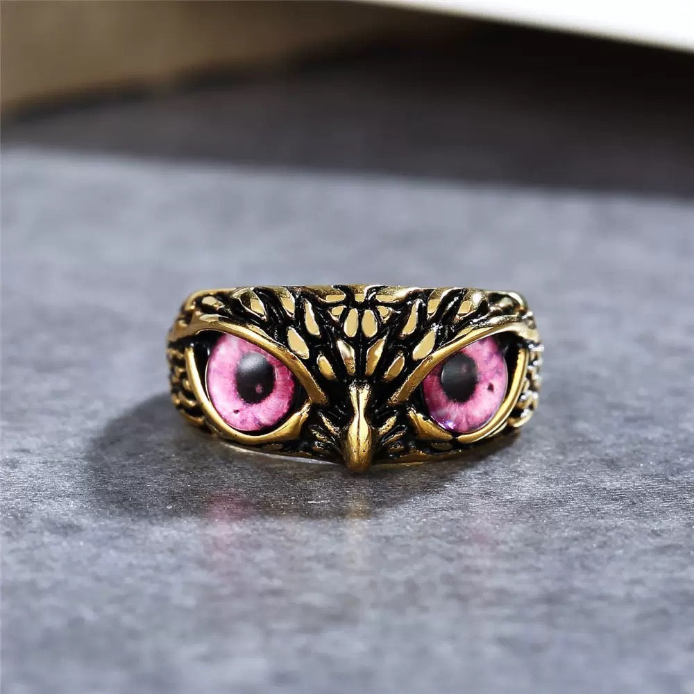 Gold owl-shaped ring with pink gem eyes on a gray surface