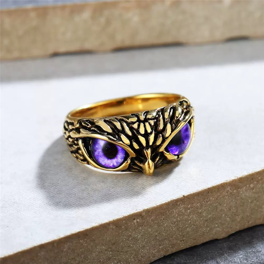 Gold owl ring with purple eyes on a white surface