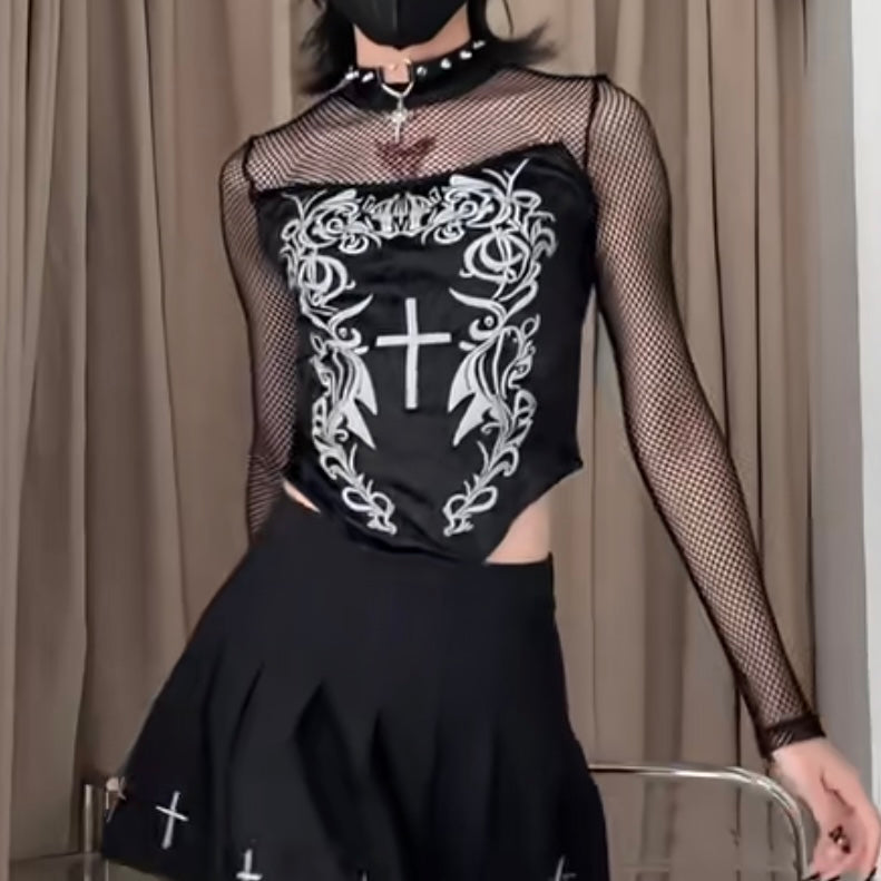 Person wearing a black outfit with white designs and fishnet sleeves against a beige curtain background