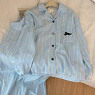 Light blue pajama set with striped pattern and black cat emblem on a beige surface.