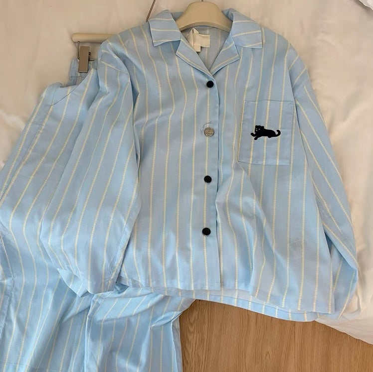 Light blue pajama set with striped pattern and black cat emblem on a beige surface.