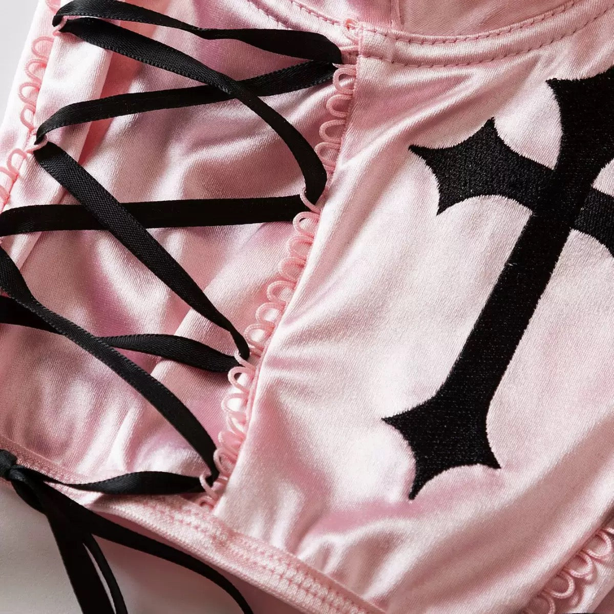 Close-up of pink shorts with black cross design and lace-up details.