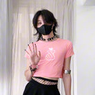 Person wearing a pink crop top with a white graphic and black pants, standing against a neutral background.