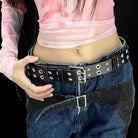 Person wearing a black studded belt with a pink top and blue jeans on a black background