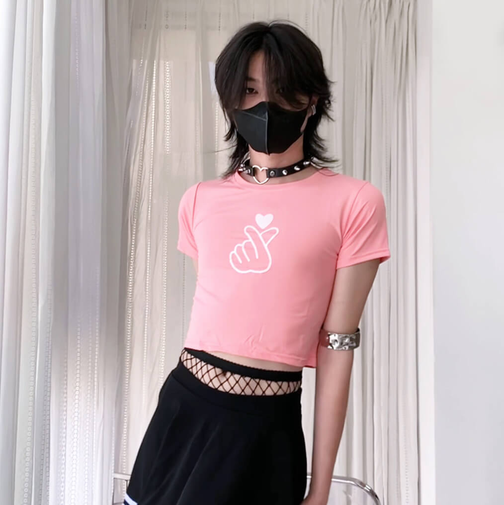 Person wearing a pink crop top with a white graphic and black pants against a neutral background