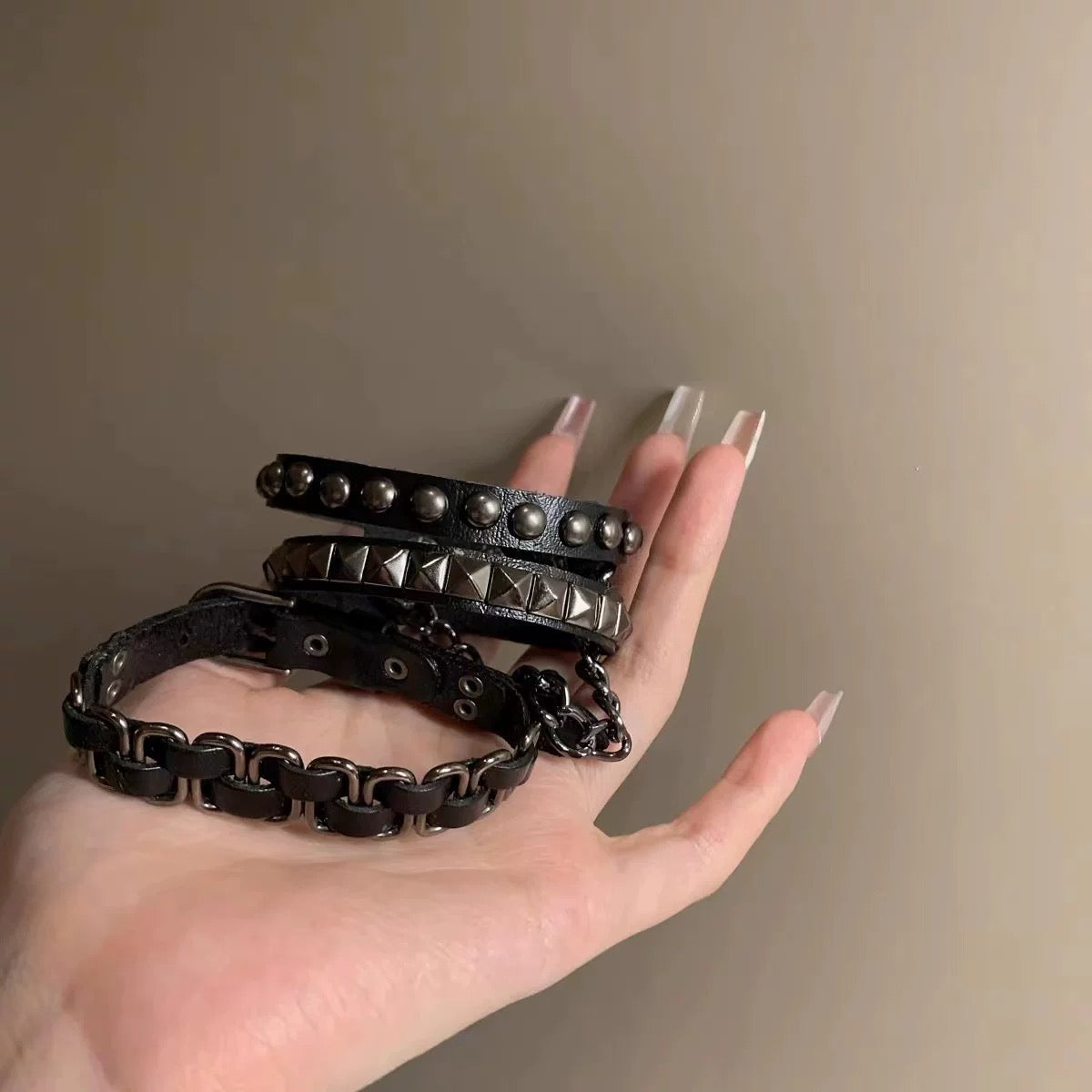 Hand holding three black punk pu leather bracelets set with various designs against a neutral background