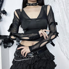 Person wearing a black outfit with sheer sleeves and ruffled skirt against a white background