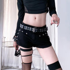 Person wearing black shorts with studs, fishnet stockings, and striped gloves against a white curtain background.