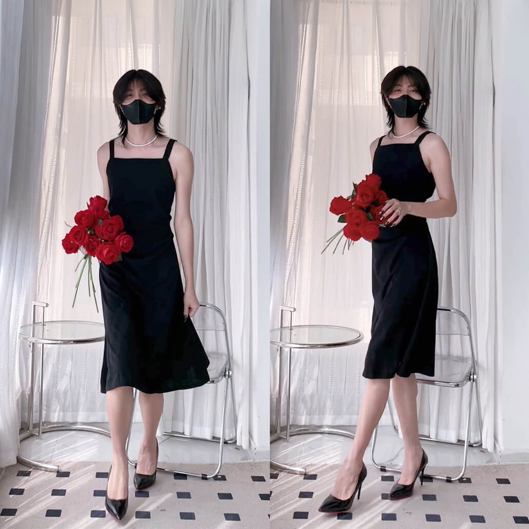 Femboy in a black dress holding red flowers in front of white curtains