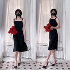 Femboy in a black dress holding red flowers in front of white curtains
