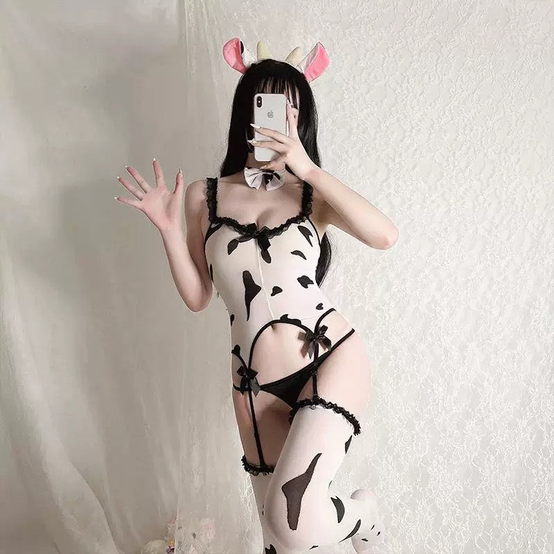Person wearing a cow print lingerie set with black lace details, taking a mirror selfie.